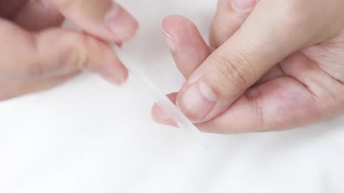 Nahaufnahme einer Frau, die Fingernägel mit einem Glaswerkzeug feilt, die Nägel präzise formt und glättet