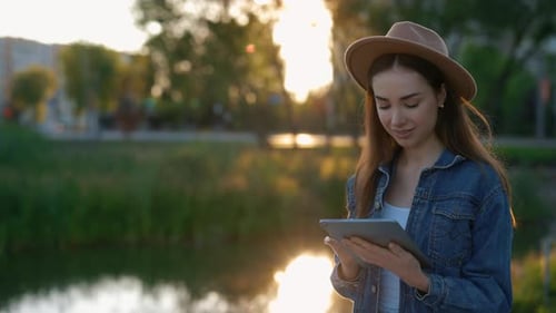 Beautiful Caucasian Woman Using Digital Tablet Computer Texting Walking Near the Local Lake Texting