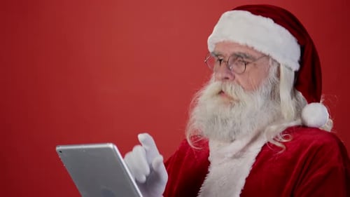 Cheerful Santa Claus Reading Wish List on Tablet