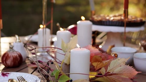 Beautiful Thanksgiving festive fall table setting with white burning candles and autumn leaves close