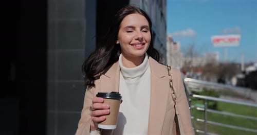 Close Up of Young Business Woman is Walking on the Street and Drinks Coffee and Using Smartphone