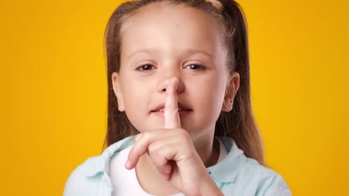 Criança feliz fazendo um gesto de silenciar contra um fundo amarelo brilhante