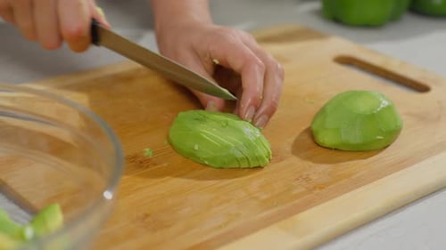 Adult Slicing Ripe Avocado on Wooden Board