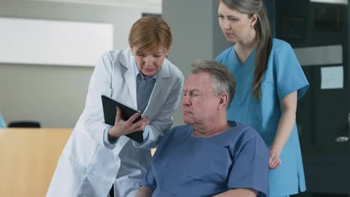 In the Hospital Female Doctor Shows Tablet Computer to Elderly Patient, Explaining his Condition. M