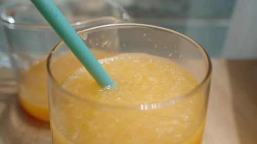 Using a blue straw, I drink orange juice with pulp, seen from a top-down view.