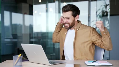 Angry man working at laptop in office