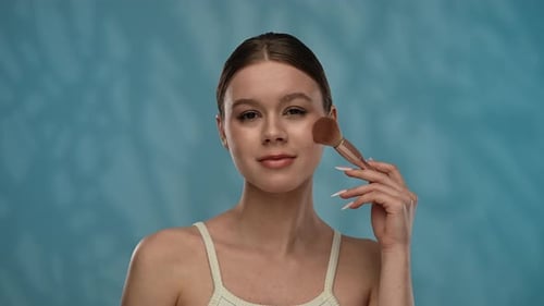 Young Woman with Makeup Posing at Camera in Studio Playfully Smiling Touching Applying Blushes with