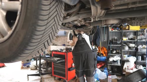 Professional Auto Mechanic Working Underneath a Lifting Vehicle at Garage