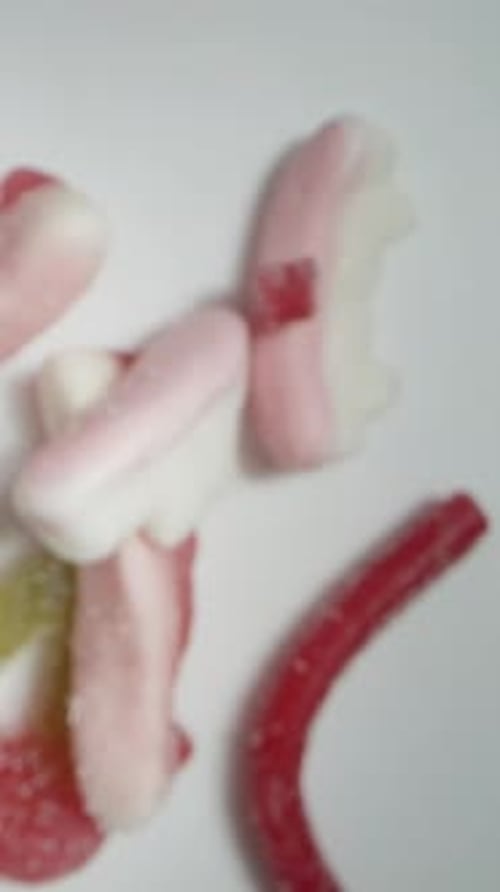 Vertical video. The camera descends downward as the mix of assorted gummy candies falls.