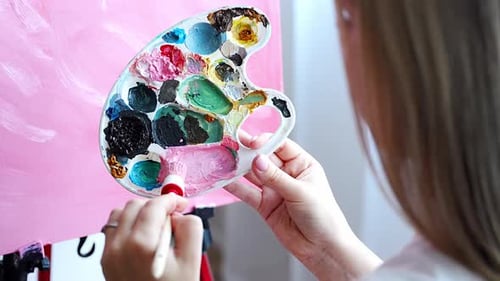 Back View of Young Woman Artist with Palette and Brush Sitting and Painting Abstract Pink Picture on