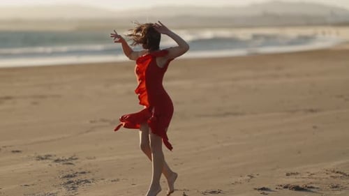 A Young Woman in Red Dress Dancing on Sandy Beach