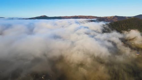 Aerial View of Vibrant Landscape of Foggy Clouds Covering Mountain Hills and Small Scattered Village