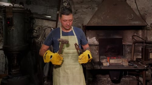 Man Holding Hammer and Tongs in Blacksmith Workshop