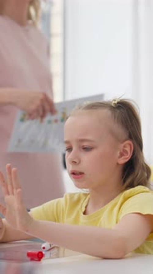Young Girl Counting on Her Fingers at a Kitchen Table with Adult in Background