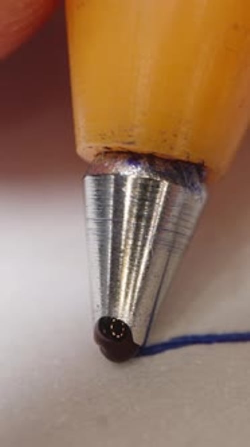 Vertical video. Ballpoint pen in hand, macro shot, ink flows through the ball at the end.