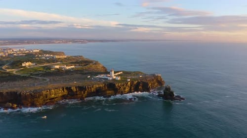 Fliegen Sie über den Leuchtturm an der Küste mit Wellen, die an der Klippe krachen.