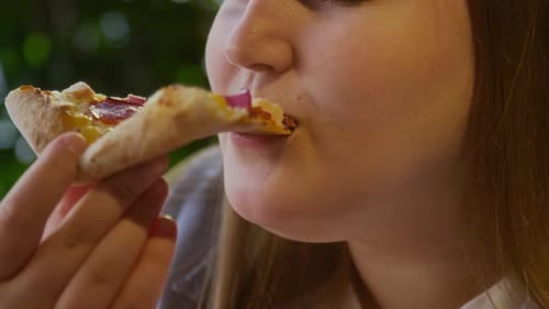 Close up of Young Girl Taking Bite of Slice of Pepperoni Pizza in cafe