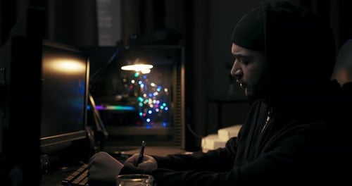 Man in Black Jacket Sits at Computer Desk in Dark Room