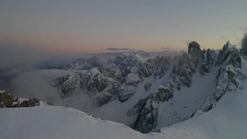 Snow covered hillside slope establishing aerial rising view Tre Cime harsh mountainous valley landsc