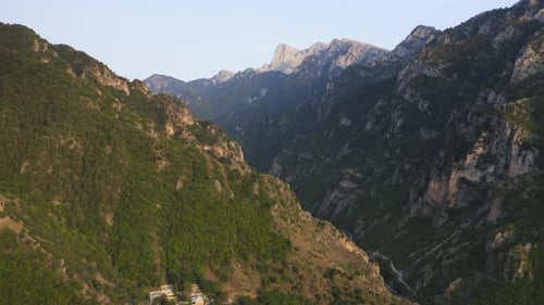 An aerial drone reveal of a canyon with a river flowing below and mountain peaks in the background