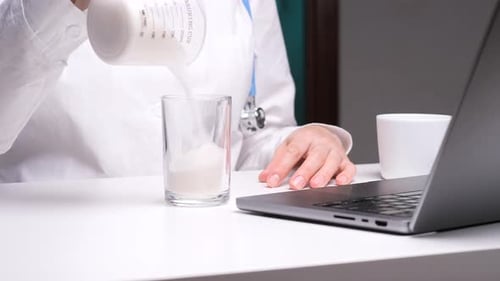 White-Coated Person Pours White Liquid Into Glass