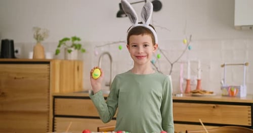 Portrait of Smiling Boy Child in Bunny Ears Holding Multicolored Chicken Egg During Easter at Home