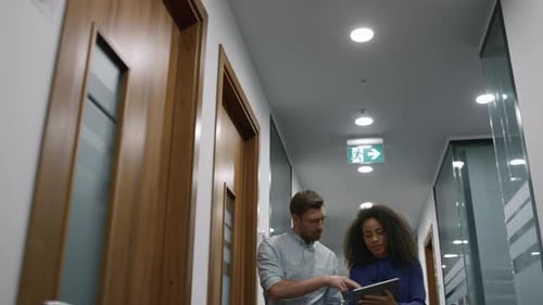 Multhiethnic Business Couple Talking Financial Project Using Tablet Computer in Office Corridor
