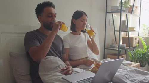 Couple Having Breakfast in Bed and Watching Movie on Laptop