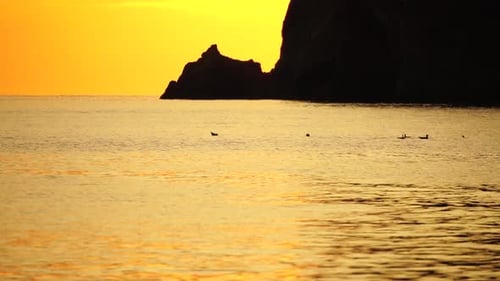 A Red Burning Sunset Over the Sea with Rocky Volcanic Cliff