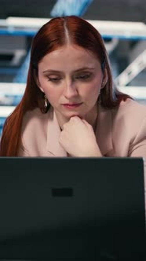 Vertikale Videoprogrammiererin am Schreibtisch im Serverraum mit Laptop
