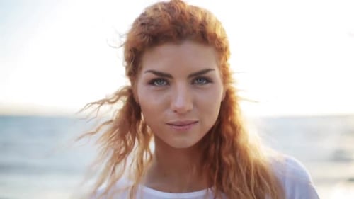 Heureuse jeune femme rousse souriant magnifiquement sur la plage au ralenti