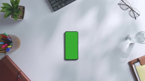 Top down view of a mock up green screen smartphone on a white office desk