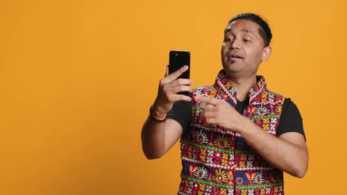Joyous Man Greeting Friend Over Online Videocall on Cellphone Studio Background