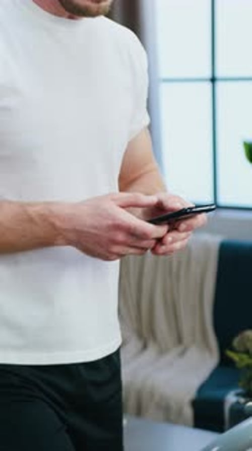 Close Up of Hands Man Uses Smartphone During Morning Home Workout on Running Track While Stepping on
