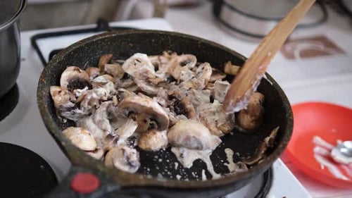 Person stirring sauteed mushrooms in skillet with spatula