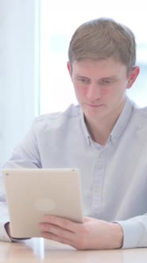 Young Man Using Tablet and Celebrating Success Indoors