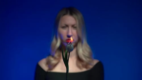 Unscharf: junge schöne blonde Frau mit üppigen roten Lippen, die eine brennende weiße Tulpenblüte hält