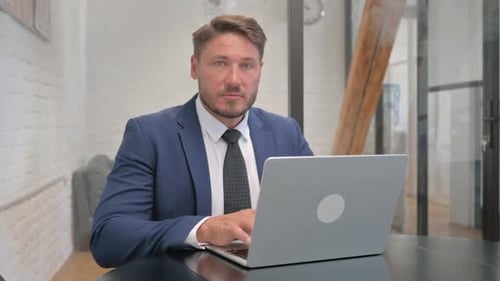 Mature Adult Businessman Looking Seriously at Camera in Office