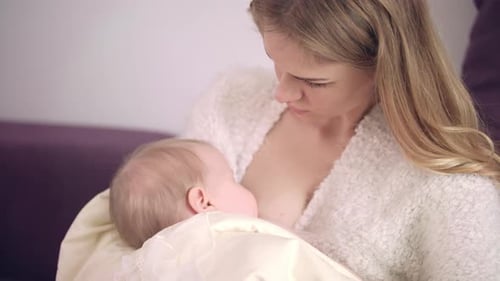 Loving Mother Breastfeeding Baby Indoors in Soft Light