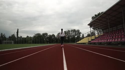 A young woman is rope jumping in the stadium. she is alone in the shot. woman is wearing a white swe