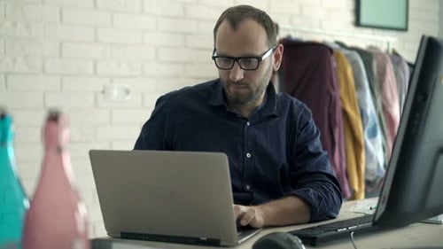 Junger Mann arbeitet an Laptop und PC und sitzt am Tisch