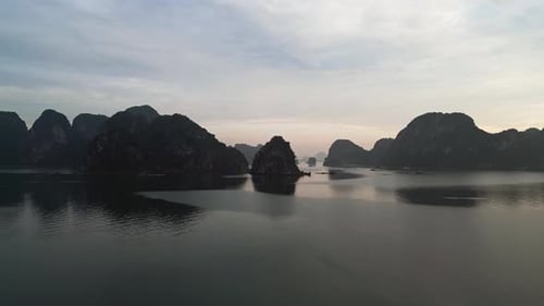 Karst islands in shadow across calm ocean water under light haze and sunset sky aerial drone view