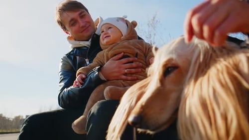 Man holding baby petting dog outside on sunny day