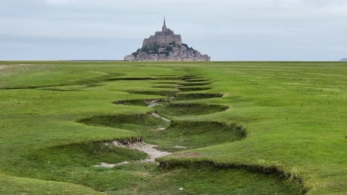 Low-altitude drone flight over green fields near Mont-Saint-Michel