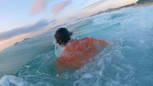 Sunrise bodyboarding. Young man appears from water and shakes his head after passing ocean. Surfer w