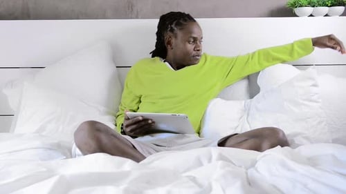 Man Relaxing in Bed Using Tablet Device
