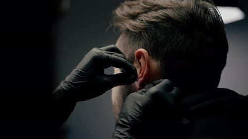 Tattoo piercing studio - a woman makes an ear piercing to a man to a guy