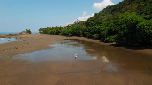 Solo traveler woman walks across empty wet sand beach on hot tropical day