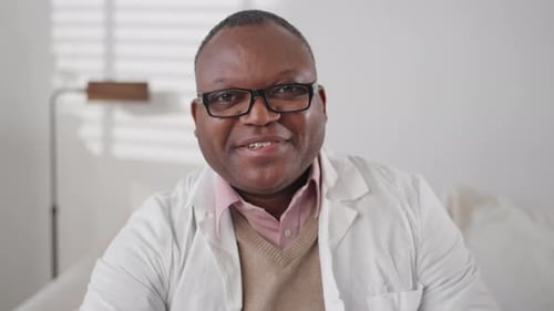 Man in White Coat Smiling Indoors at Camera