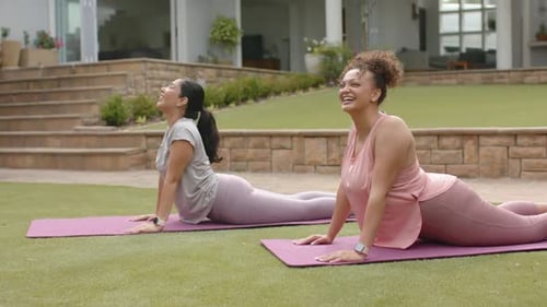 Diversas amigas siguiendo el ejemplo, sosteniendo las curvas hacia atrás a juego sobre tapetes morados en el césped, sonriendo